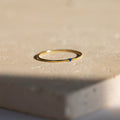 The Thin Mini Birthstone Ring, featuring a delicate blue stone, sits on a beige textured surface—an elegant piece of minimalist jewelry and an ideal Christmas gift.
