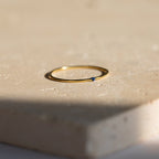 The Thin Mini Birthstone Ring, featuring a delicate blue stone, sits on a beige textured surface—an elegant piece of minimalist jewelry and an ideal Christmas gift.