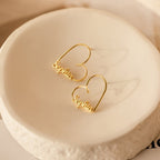 London Heart Name Earrings in gold, featuring a heart-shaped hoop customized with the name Sophia, beautifully displayed on a textured round white dish—ideal as a personalized gift.