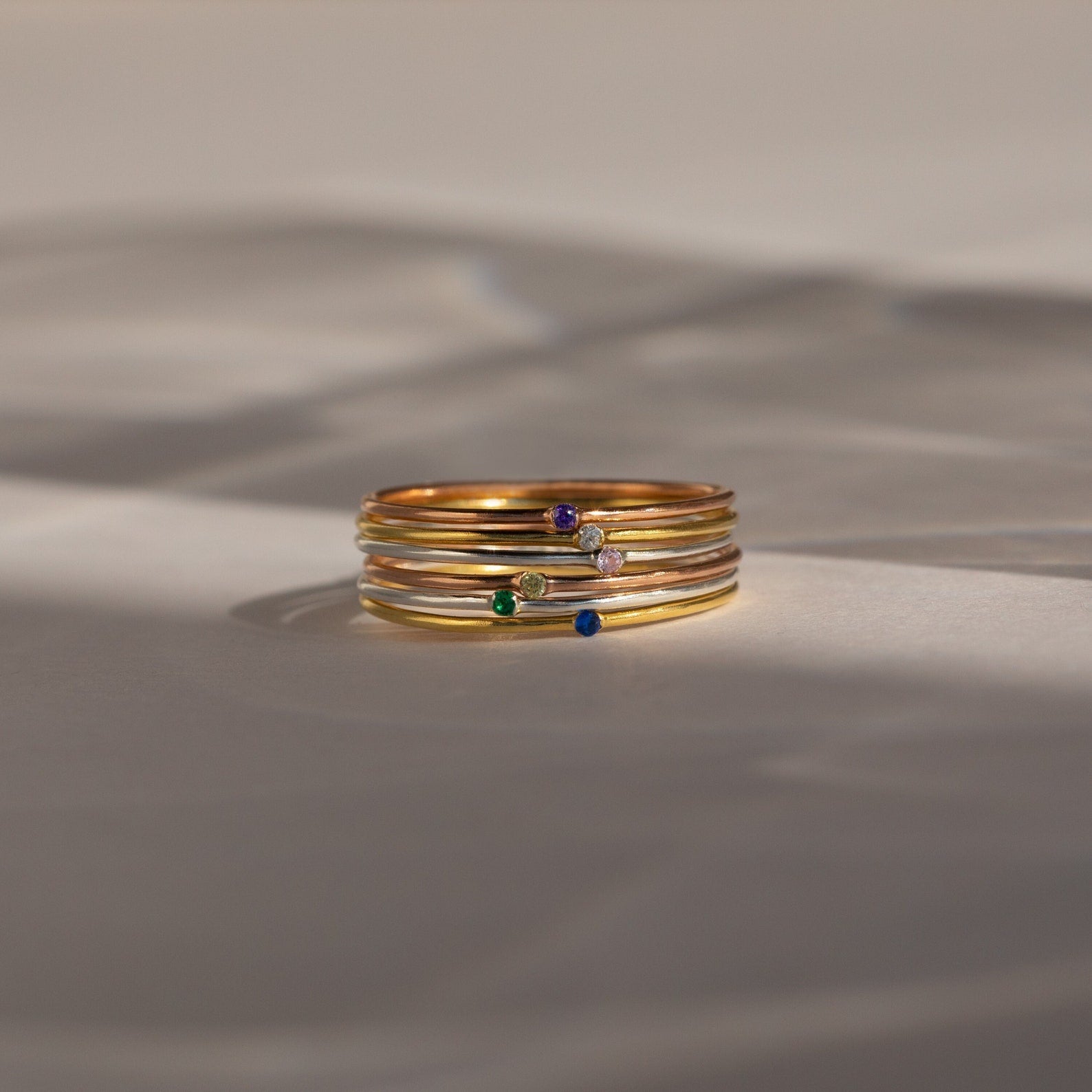 A stack of Thin Mini Birthstone Rings, featuring small colorful gemstones, rests on a soft neutral background—perfect minimalist jewelry and an ideal Christmas gift.