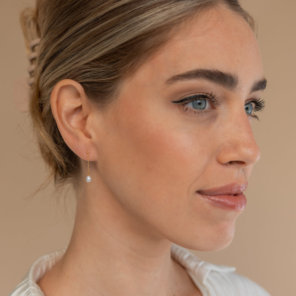 Woman with blue eyes and light makeup wears the Isha Pearl Drop Earrings in 18K Gold, looking to the side.
