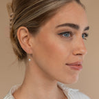 Woman with blue eyes and light makeup wears the Isha Pearl Drop Earrings in 18K Gold, looking to the side.