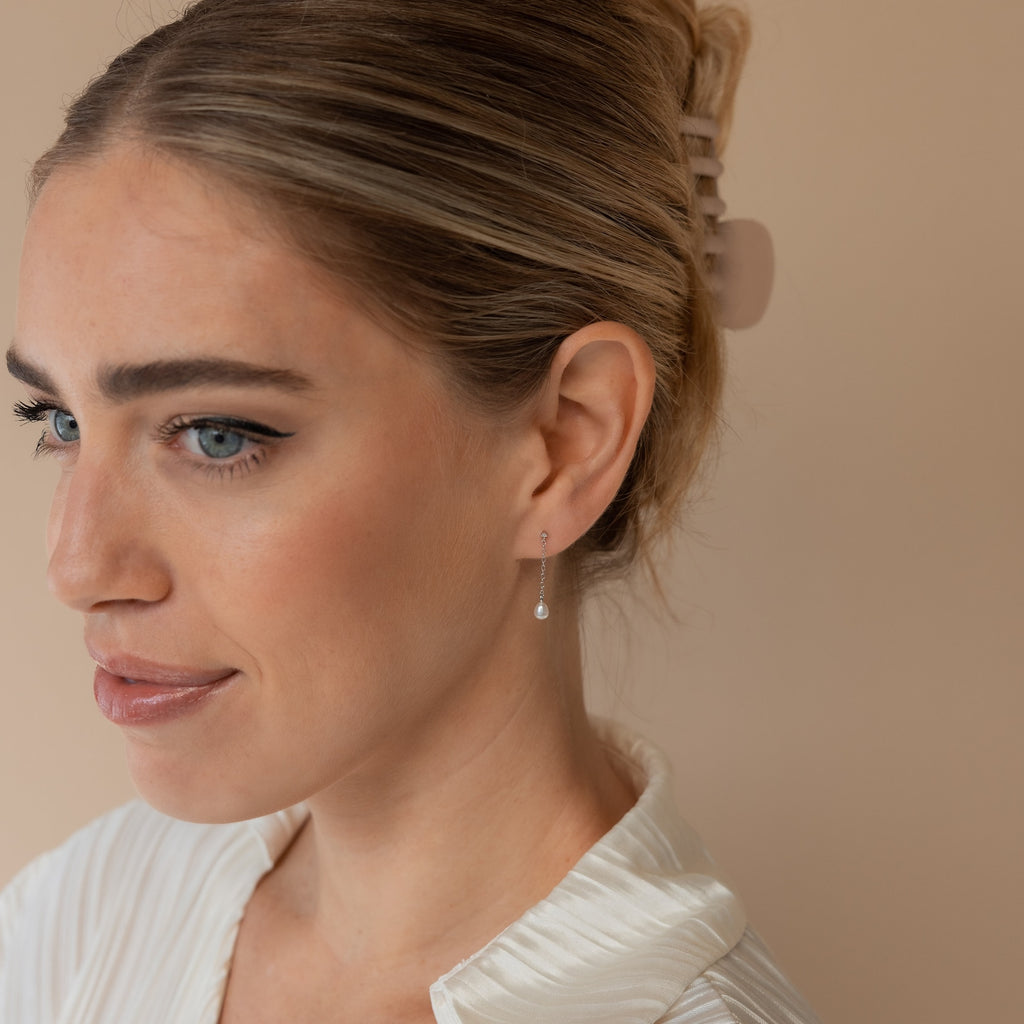 A woman with light hair in a claw clip and a white top looks to the side, showcasing elegant Isha Pearl Drop Earrings.