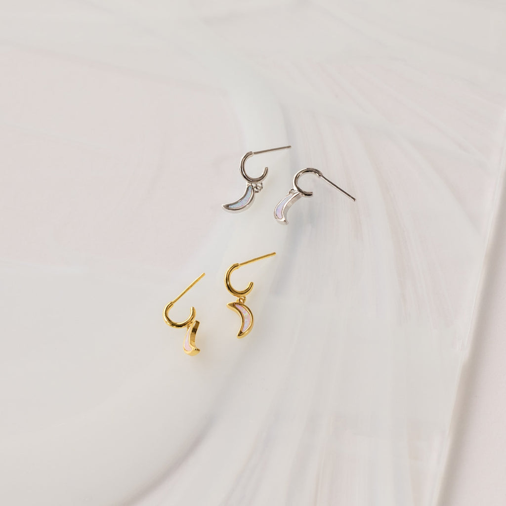 Opal Moon Mini Hoops—crescent-shaped huggie earrings in gold and silver, shown on a white textured surface—are perfect for creating a stunning earring stack.
