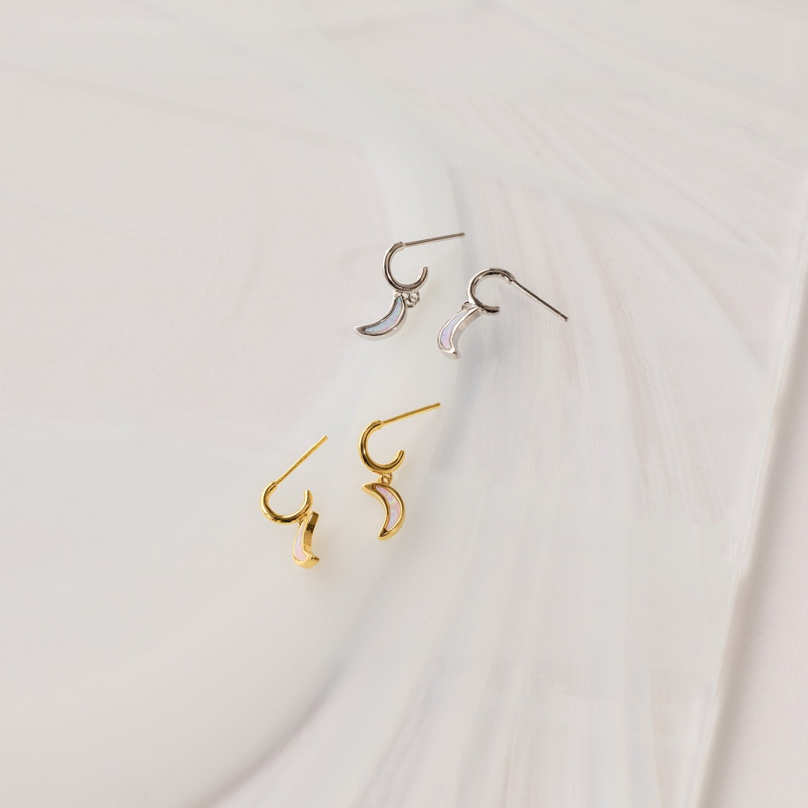 Opal Moon Mini Hoops—crescent-shaped huggie earrings in gold and silver, shown on a white textured surface—are perfect for creating a stunning earring stack.