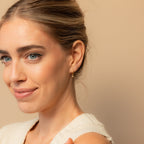 Smiling woman with blue eyes and light hair wears a cream-colored top and Ericka Diamond Huggies in Sterling Silver.