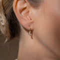 Close-up of a woman's ear wearing Opal Moon Mini Hoops, small gold crescent moon-shaped huggie earrings perfect for stacking.