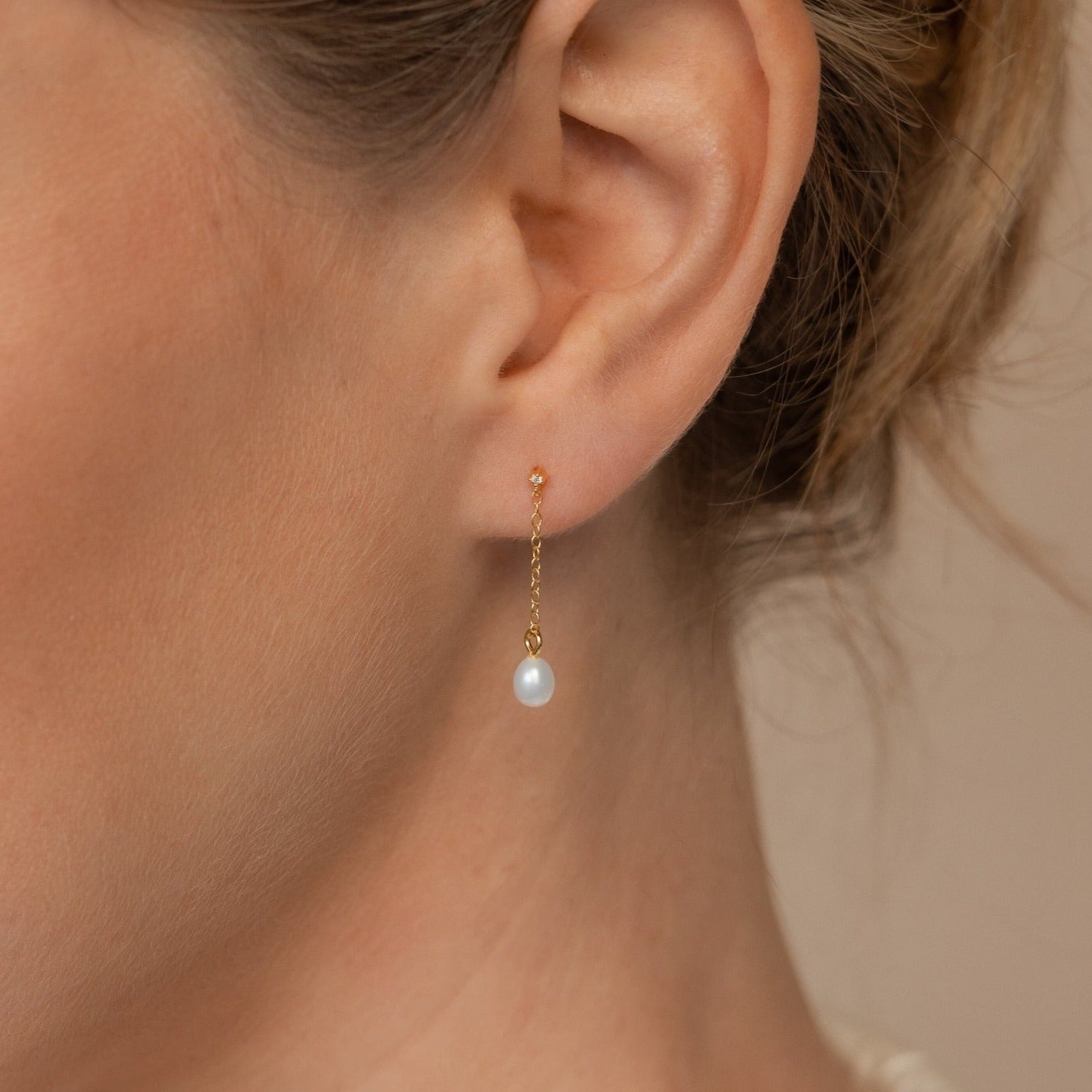 Close-up of an ear wearing the Isha Pearl Drop Earrings in 18K Gold, featuring a delicate gold chain and a graceful white pearl drop.