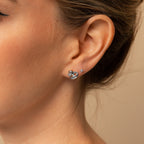 Close-up of a woman's ear wearing Heart Knot Studs—silver earrings with a delicate knot design—paired with a small crystal diamond charm.