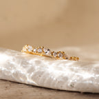 The Verity Diamond Ring, a delicate gold cluster band adorned with clear diamonds, rests on a textured white surface.