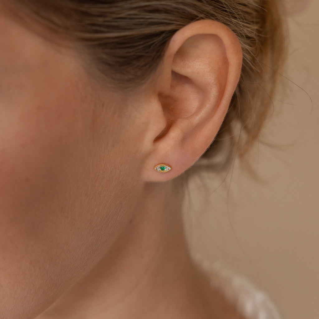 Close-up of a woman’s ear wearing Haven Emerald Eye Studs, which feature a small green emerald stone.