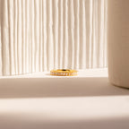 The Alicia Pearl Inlay Band, a minimalist ring featuring delicate pearls, is showcased on a neutral surface with soft natural light highlighting its elegant design against a textured backdrop.