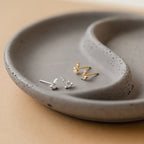 A pair of Flora Marquise Studs in Sterling Silver is displayed on a speckled gray ceramic dish.