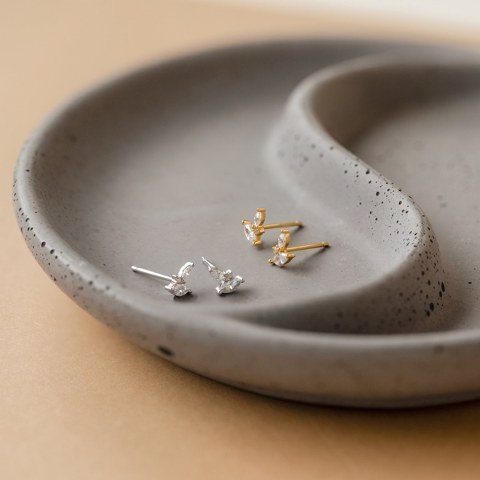 A pair of Flora Marquise Studs in Sterling Silver is displayed on a speckled gray ceramic dish.