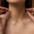 A woman wears the Larissa Emerald Station Necklace, a dainty, vintage-inspired piece featuring small green and white gemstone charms around her neck.