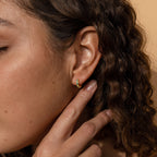 A close-up of a woman's ear wearing the Opal Inlay Huggies Set, showcasing the hoops' vibrant opal colors.