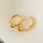 Peridot Heart Huggies—gold hoop earrings with heart-shaped peridot stones, shown on a cream fabric background. Perfect minimalistic jewelry to elevate your style.