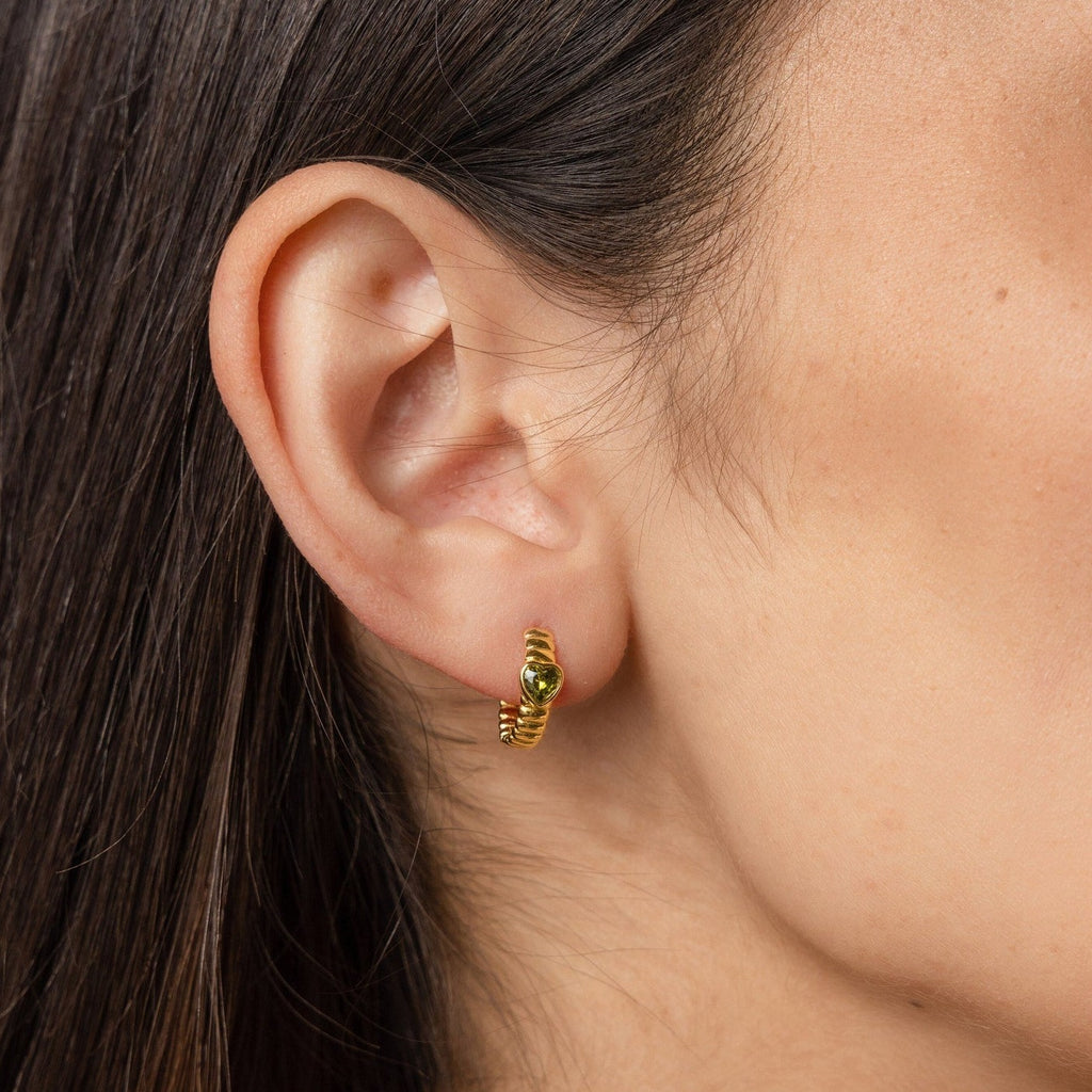 A close-up of a woman's ear wearing Peridot Heart Huggies—minimalistic earrings with a small green gemstone, perfect for those who love understated elegance.
