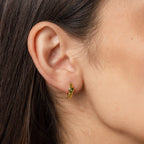 A close-up of a woman's ear wearing Peridot Heart Huggies—minimalistic earrings with a small green gemstone, perfect for those who love understated elegance.