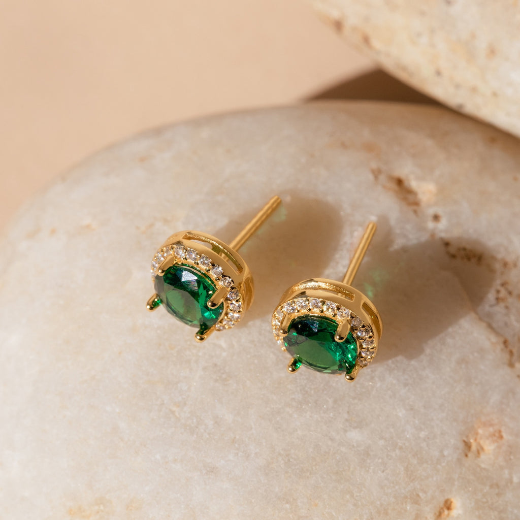 Halo Birthstone Studs featuring green gemstones and small diamonds, vintage-inspired earrings showcased on a smooth beige stone background.