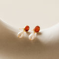 A pair of Carnelian Pearl Earrings rests on a white surface, highlighting the beauty of earthy jewelry.