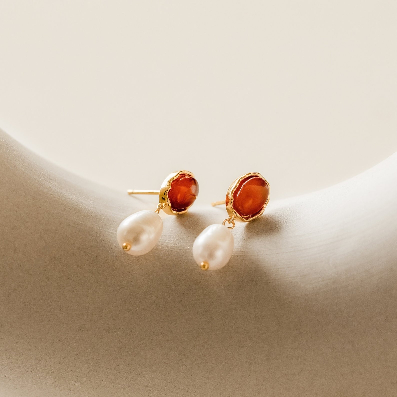 A pair of Carnelian Pearl Earrings rests on a white surface, highlighting the beauty of earthy jewelry.