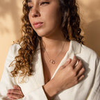 A woman with curly hair wears a white blazer paired with the Engraved Interlocking Necklace—an elegant and meaningful choice, perfect as an anniversary gift.
