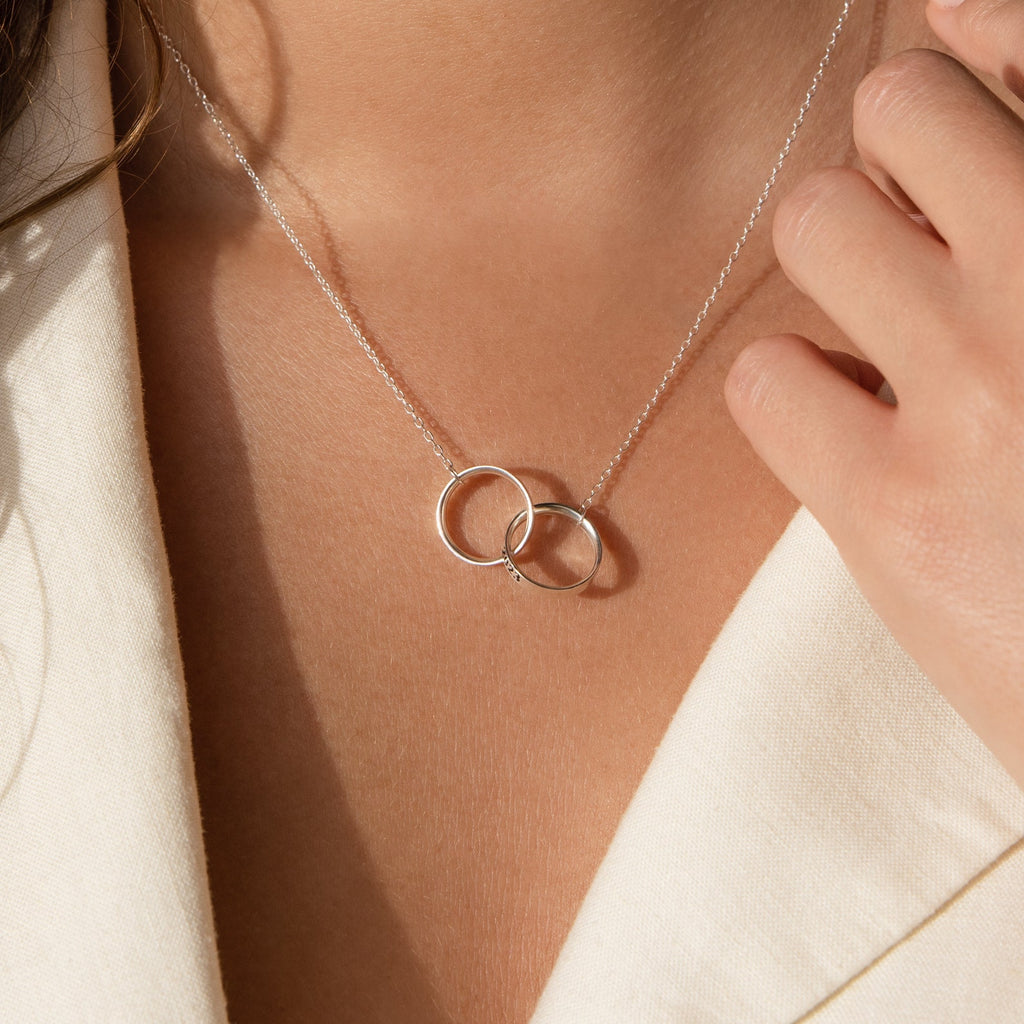 Close-up of a woman wearing the Engraved Interlocking Necklace with two silver rings—a perfect anniversary gift.