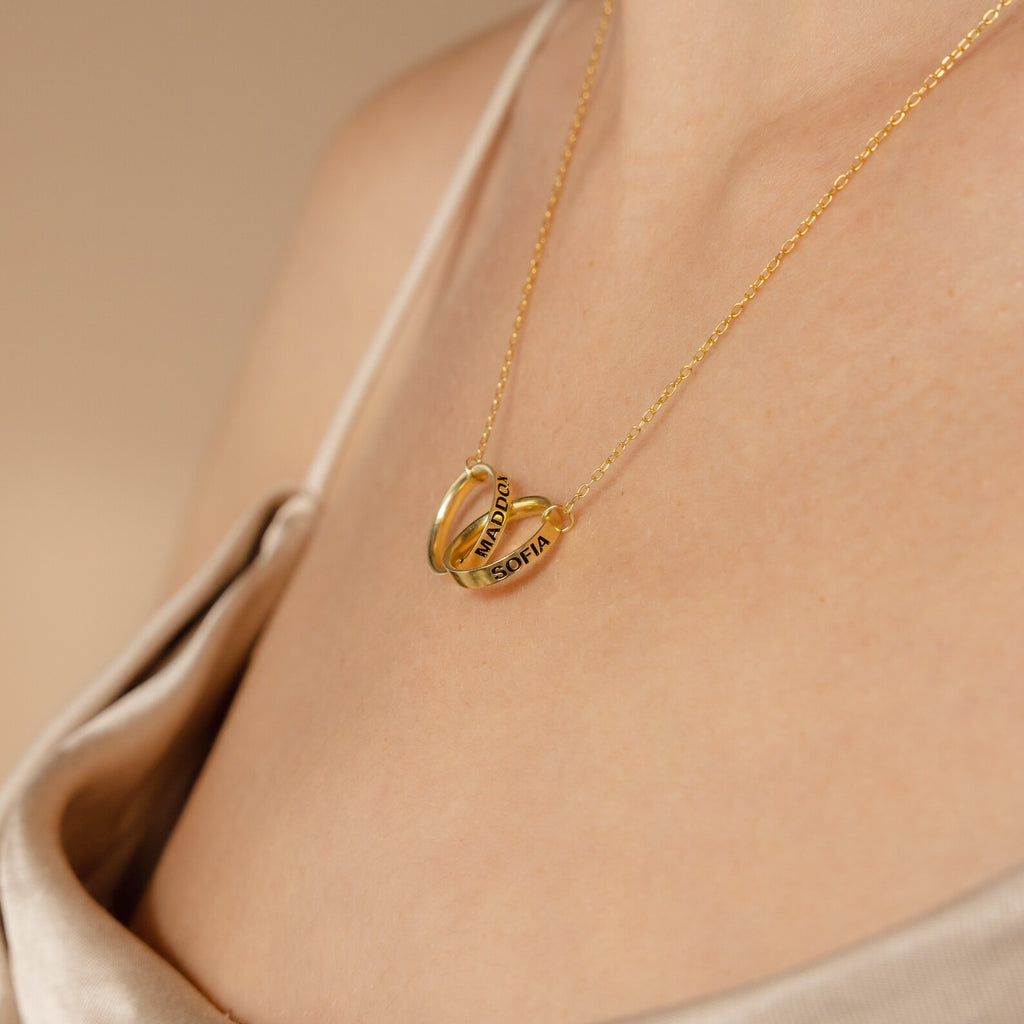 A woman wears the Engraved Interlocking Necklace featuring two personalized rings engraved with MATILDA and SOFIA—an elegant anniversary gift.