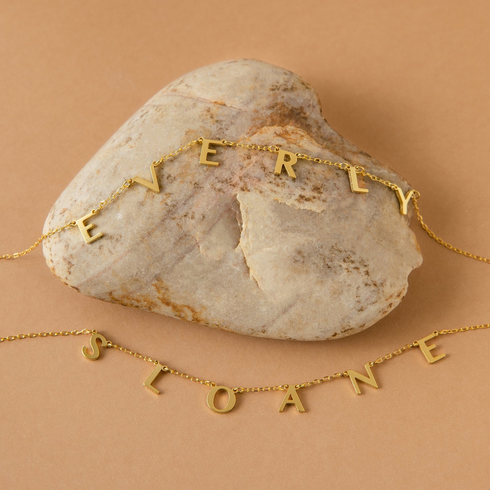 The Apollo Letter Name Necklace, shown with gold minimalist letter charms spelling EVERLY and SLOANE on a heart-shaped stone, is the perfect custom initial necklace for a personal touch.