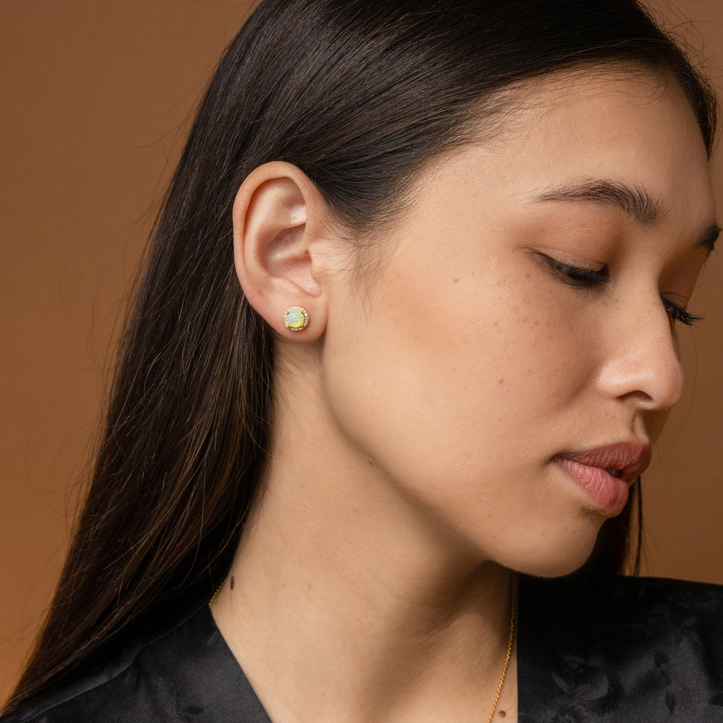 A woman with long dark hair wears Halo Birthstone Studs, gazing down against a brown backdrop.