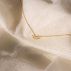 Marquise Birthstone Necklace featuring a small opal and diamond pendant, showcased on shimmery cream fabric.