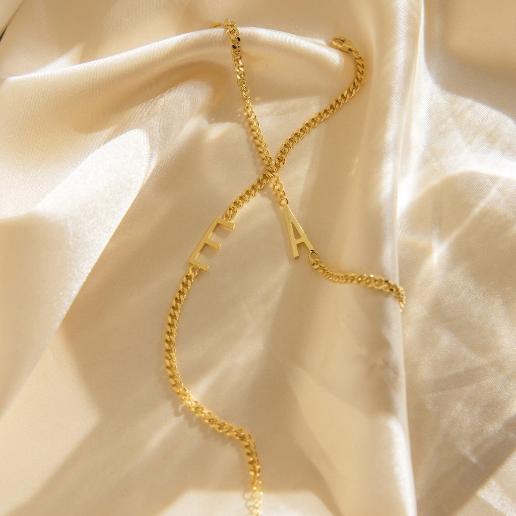 Large Letter Bracelet with personalized E and A pendants rests on soft, cream-colored satin—ideal for everyday wear or styling with a gold chain necklace for a chic ensemble.