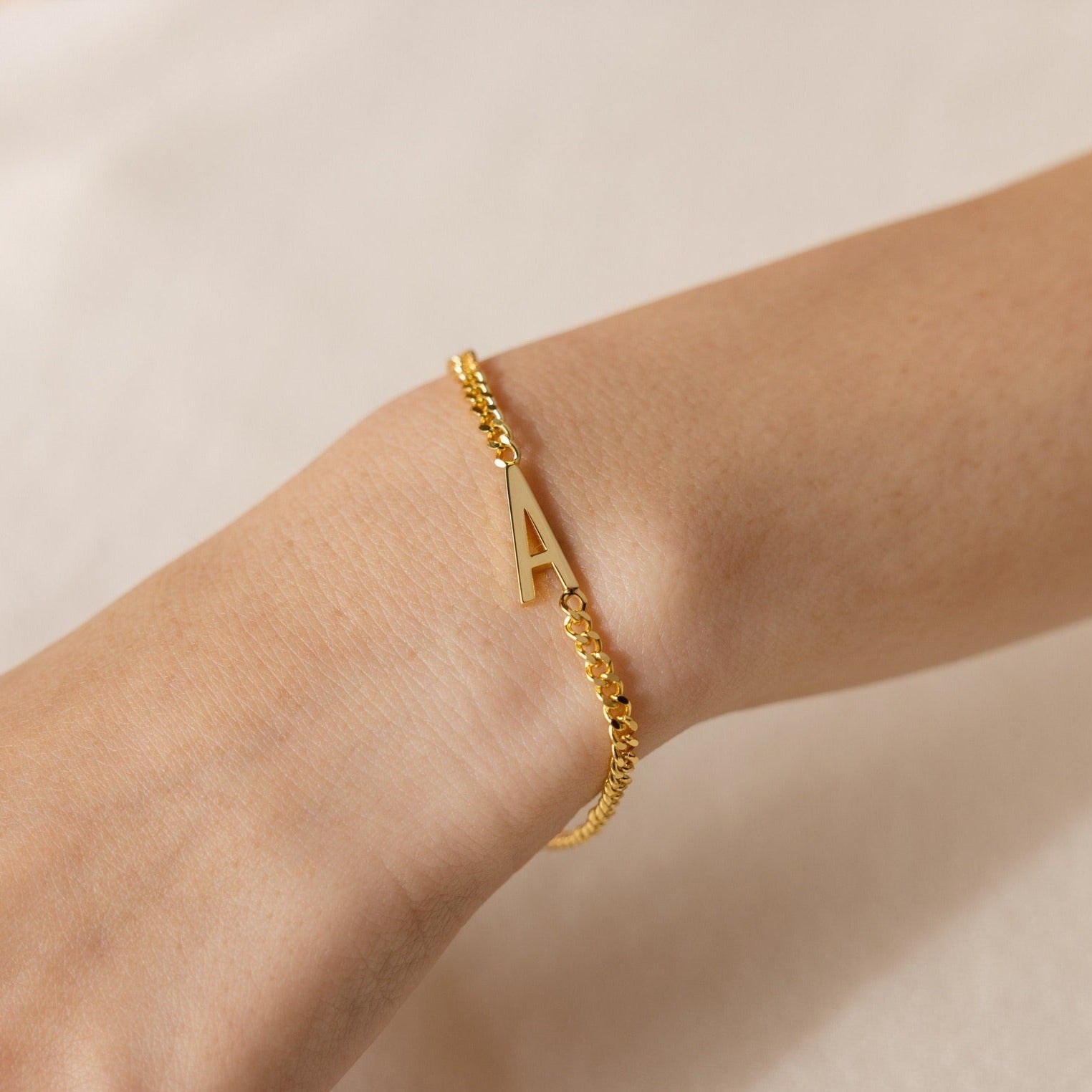The Large Letter Bracelet with a gold "A" charm adorns the wrist against a neutral backdrop—a chic, personalized accessory for everyday wear.