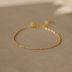 The Singapore Twist Bracelet shines on a neutral beige surface, ideal for those who appreciate dainty bracelets and minimalist elegance.