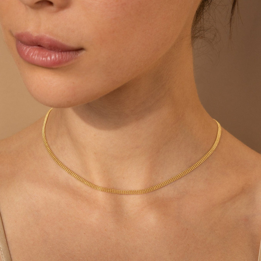 A woman wears the Tri-Stacked Beaded Necklace layered with a delicate gold chain against a neutral background—showcasing versatile jewelry style.