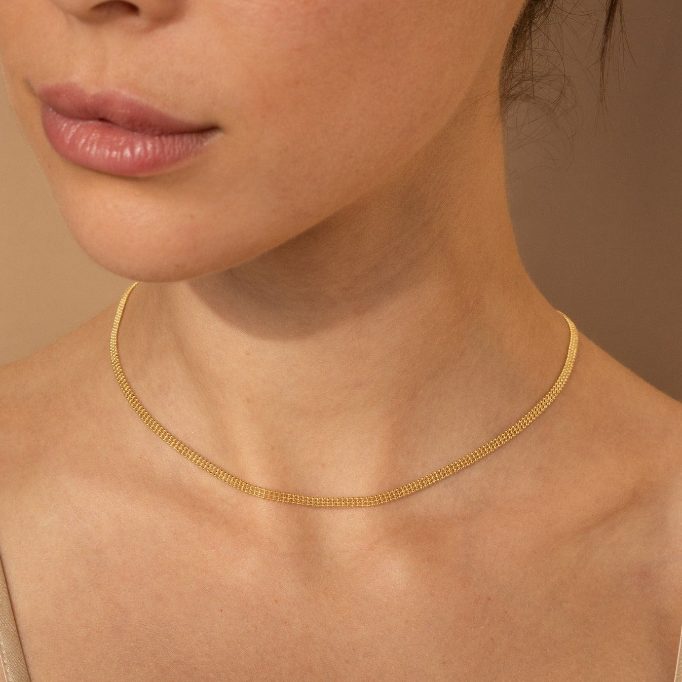 A woman wears the Tri-Stacked Beaded Necklace layered with a delicate gold chain against a neutral background—showcasing versatile jewelry style.