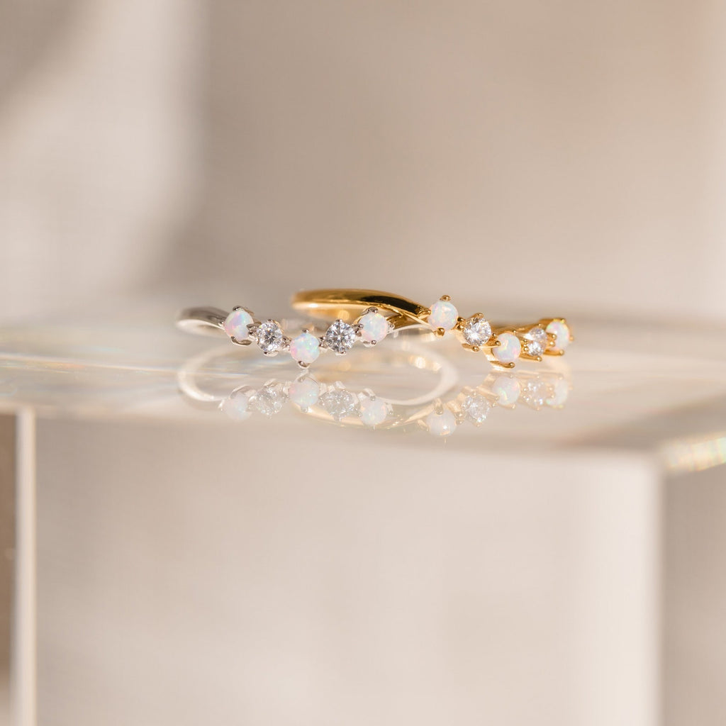 The Layla Opal Diamond Ring pairs delicate minimalism in silver and gold with opal and diamond accents, offering boho chic charm beautifully displayed on a glass surface.