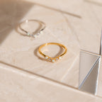 The Layla Opal Diamond Ring features a minimal gold design with a small opal and diamond, displayed on light marble next to a triangular mirror for a subtle boho chic vibe.