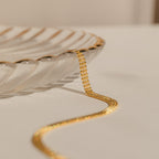 The Tri-Stacked Beaded Necklace, ideal for versatile jewelry styling, drapes over the edge of a clear, scalloped glass dish on a neutral surface.