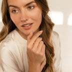 Woman with wavy brown hair in a white blouse touches her chin, showcasing the Delicate Pearl Diamond Ring on her finger.