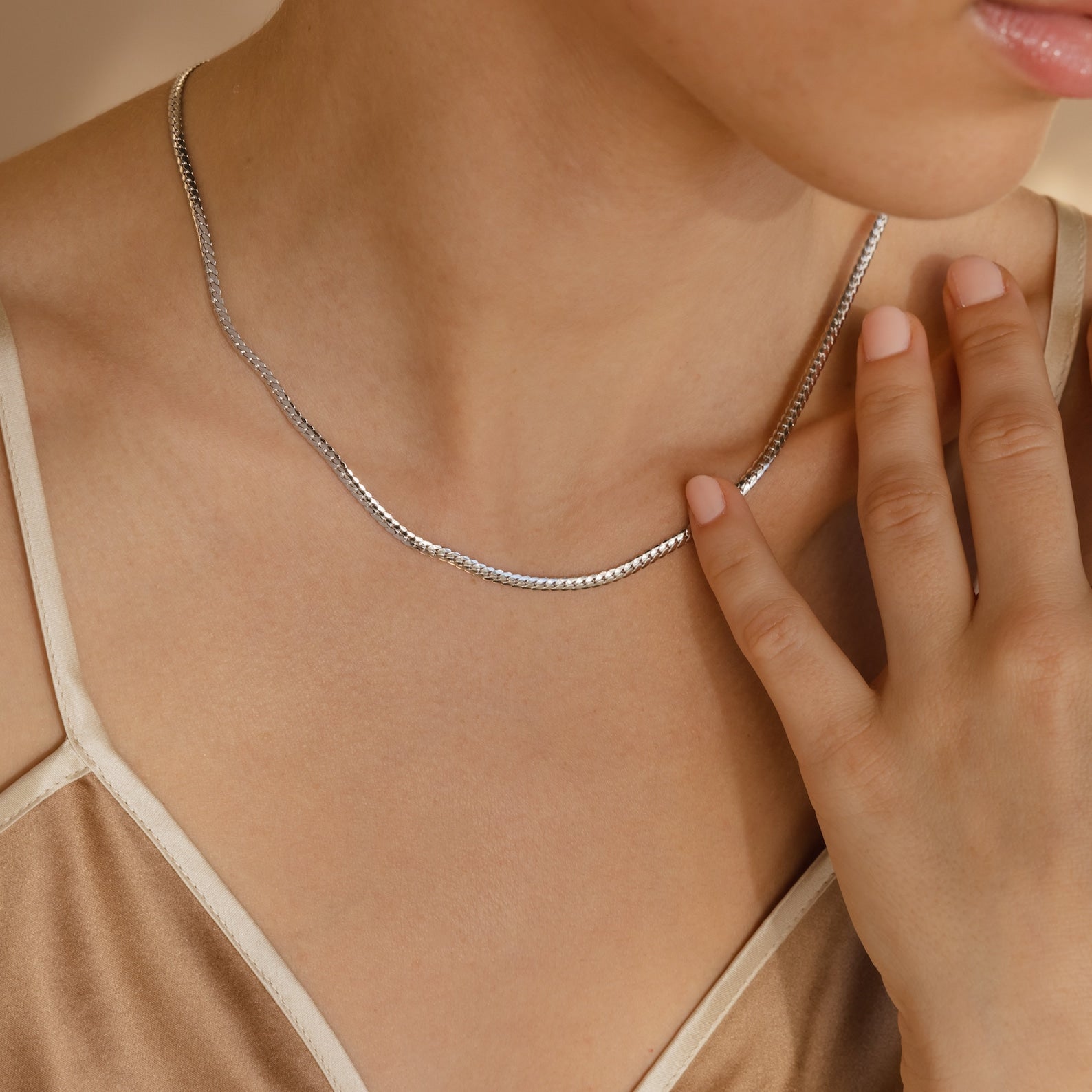 A woman in a beige satin top touches her collarbone while wearing the Thick Snake Chain Necklace—a stylish, simple silver piece that's an effortless everyday staple.