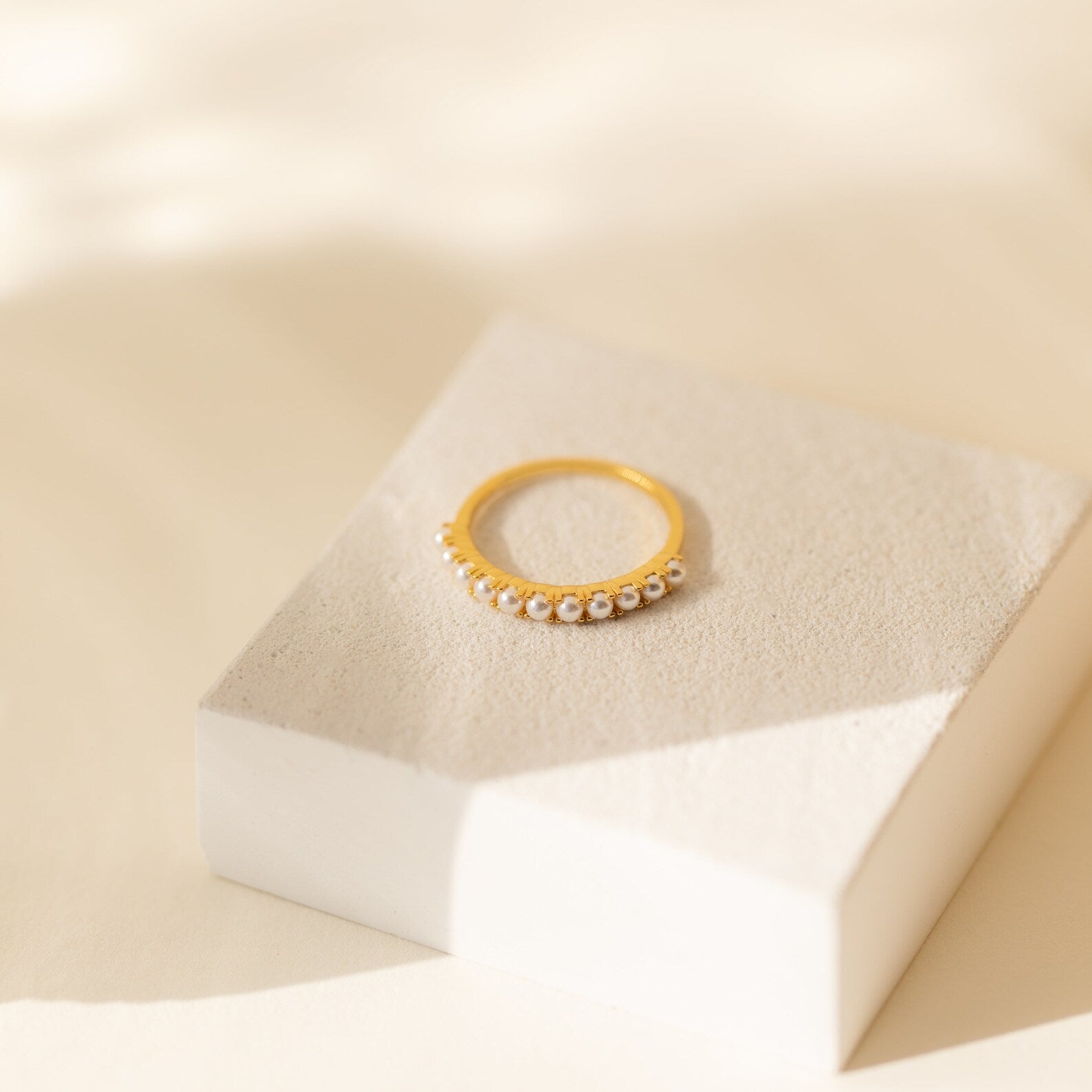 The Crescent Pearl Ring, a handmade stacking piece adorned with small pearls, is displayed on a white textured block in gentle natural light—ideal for fans of minimalist jewelry.