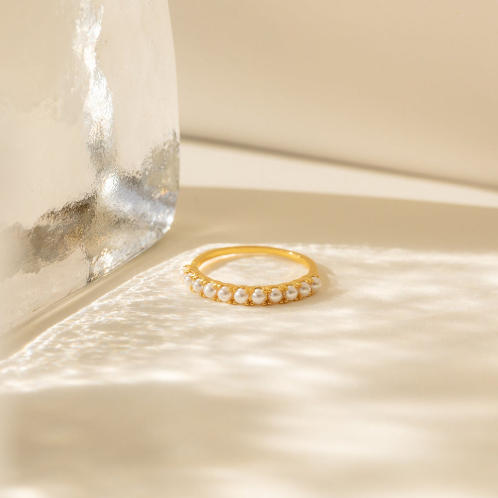 The Crescent Pearl Ring is a minimalist ring with small white pearls set in gold, shown on a cream background with soft natural light and shadows.