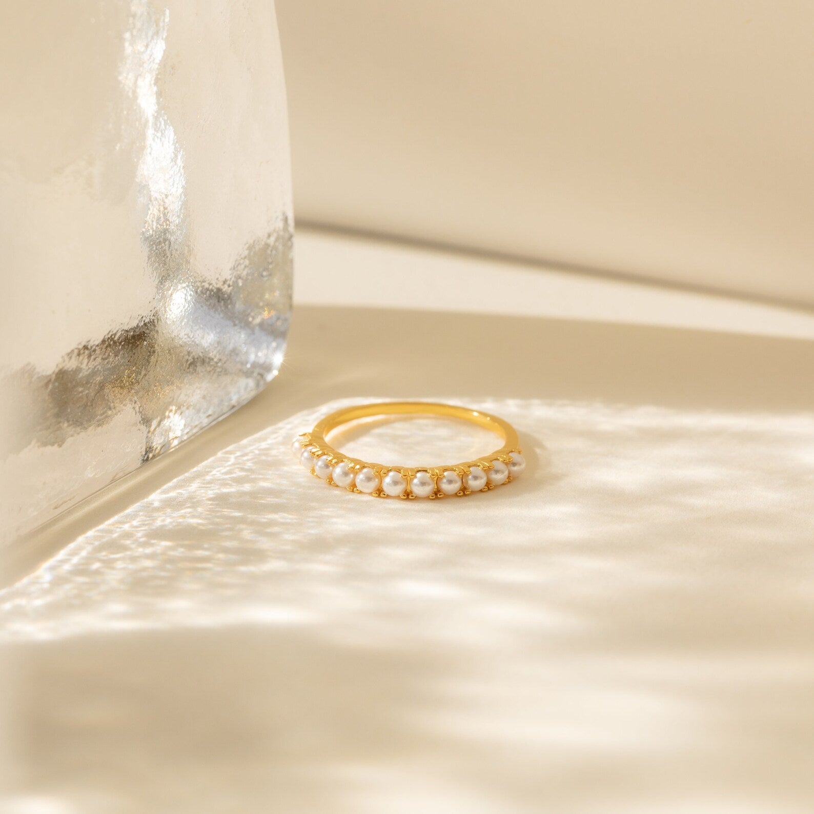 The Crescent Pearl Ring is a minimalist ring with small white pearls set in gold, shown on a cream background with soft natural light and shadows.
