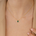 The Maia Emerald Necklace, featuring a small emerald pendant, rests elegantly on a person wearing a beige blazer.