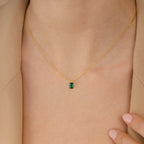 The Maia Emerald Necklace, featuring a small emerald pendant, rests elegantly on a person wearing a beige blazer.