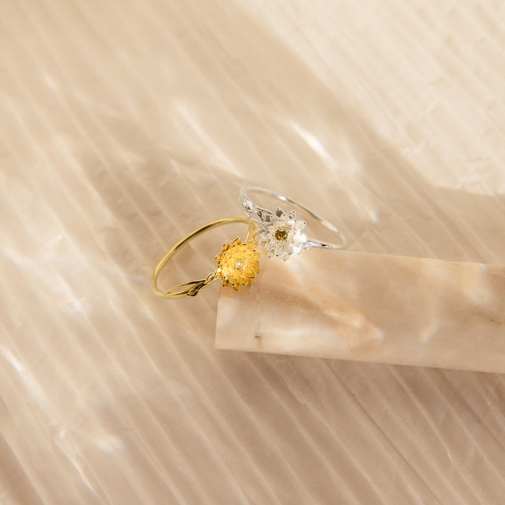 Two delicate Flower Birthstone Rings: one gold with a yellow flower, and one silver with a white flower.