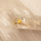 Two delicate Flower Birthstone Rings: one gold with a yellow flower, and one silver with a white flower.