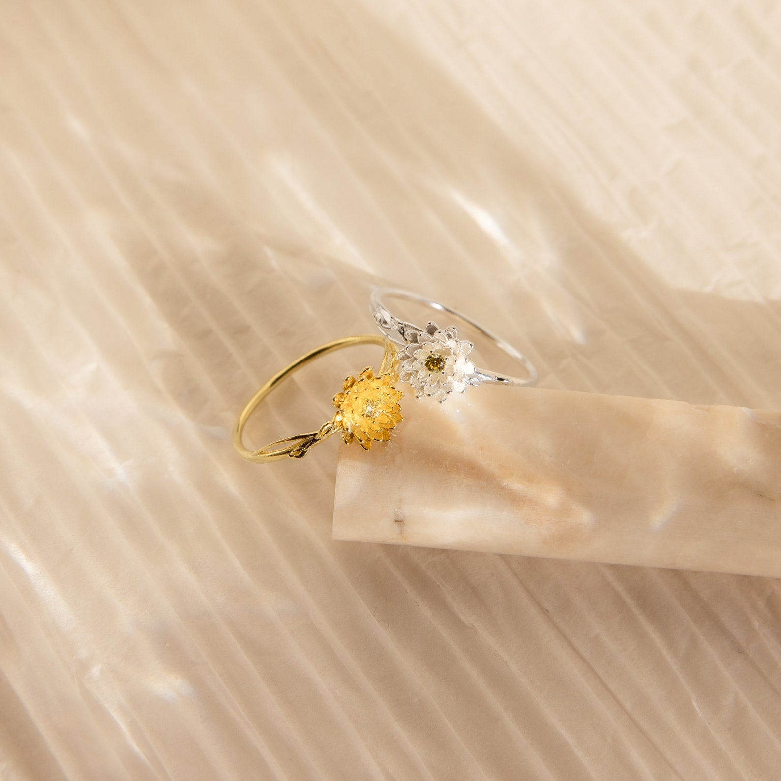 Two delicate Flower Birthstone Rings: one gold with a yellow flower, and one silver with a white flower.